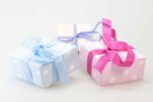 Trois petits paquets cadeaux à pois, dans des tons pastel bleu et rose, symbolisant le soin apporté au choix d'une attention pour les parents.