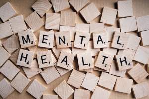 Jetons de jeu de lettres en bois formant les mots MENTAL HEALTH (santé mentale), disposés de manière organique pour symboliser la recherche d'équilibre.
