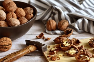 Un bol de noix, un marteau et des noix concassées sur une planche, illustrant l'action de prendre soin de sa santé par l'alimentation brute et naturelle.